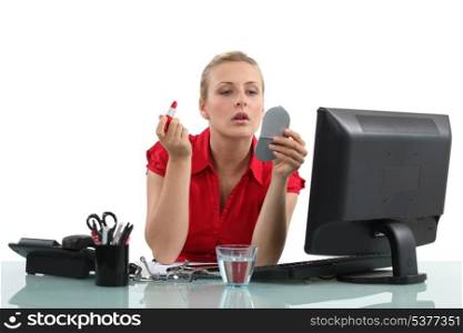 Blond woman applying lipstick in office