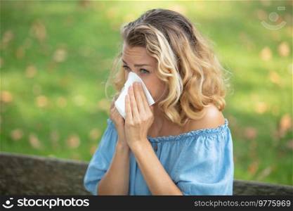 blond woman blowing nose outdoors