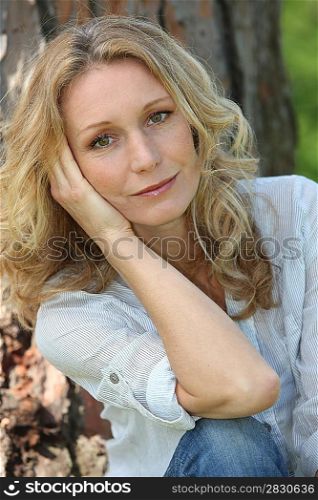 Blond woman by tree with hand on face