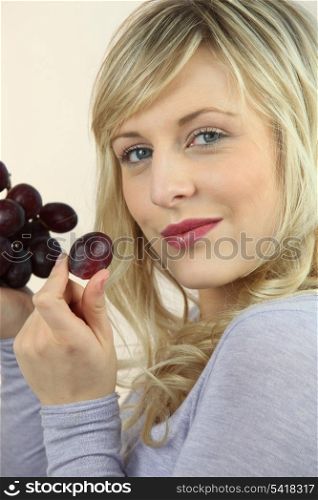 Blond woman eating bunch of grapes