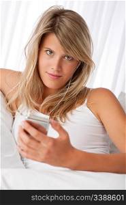 Blond woman holding mp3 player listening to music on white sofa