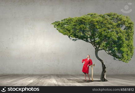 Blond woman in red coat with axe and green tree. Protect forests