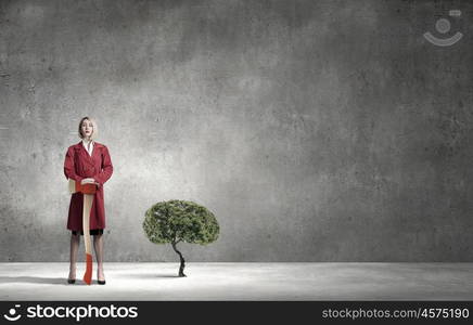 Blond woman in red coat with axe and green tree. Protect forests