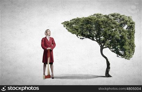 Blond woman in red coat with axe and green tree. Protect forests