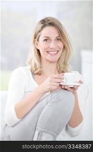 Blond woman in sofa holding coffee cup