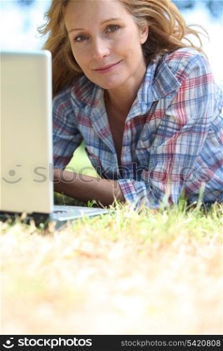 Blond woman laid on grass with laptop computer