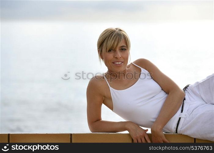 Blond woman leaning on wall by waterfront
