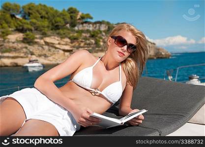 Blond woman lying on yacht reading book sunbathing on sunny day