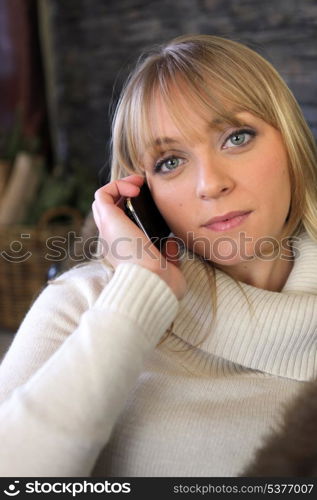 Blond woman making phone call whilst sat on cosy sofa