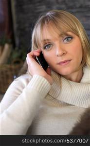 Blond woman making phone call whilst sat on cosy sofa