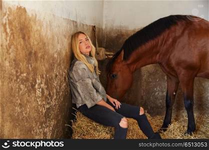 Blond woman on an indoor stable with horse. Blond woman on an indoor stable with a brown horse on straw bale