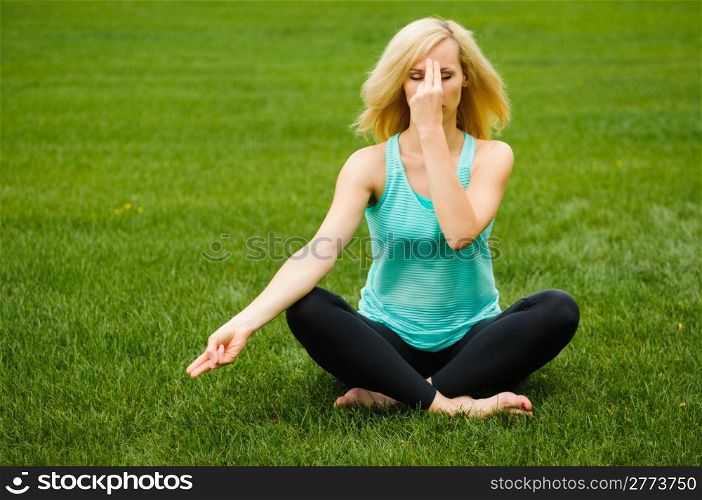 Blond woman on green grass doing yoga meditation