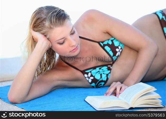 Blond woman reading a book whilst sunbathing