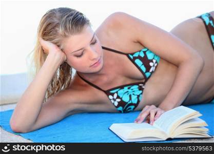 Blond woman reading a book whilst sunbathing