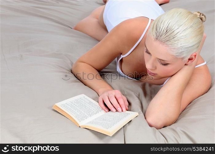Blond woman reading book in bed