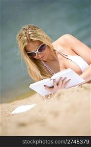 Blond woman reading book on sunny beach
