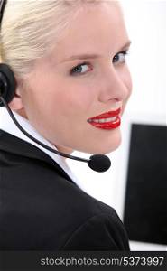 Blond woman sat by computer wearing telephone head-set