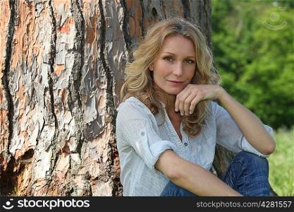 Blond woman sat by tree hand touching face
