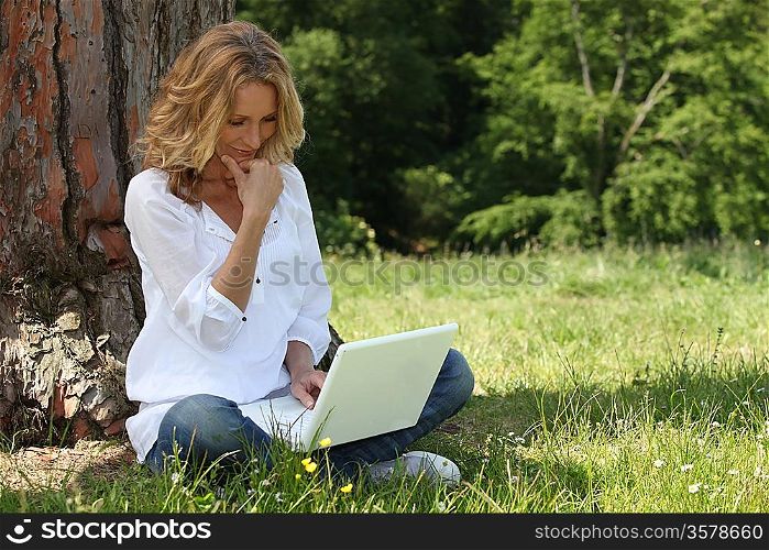 Blond woman sat by tree with laptop