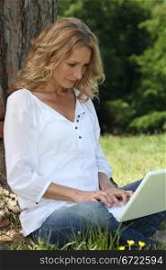 Blond woman sat by tree with laptop
