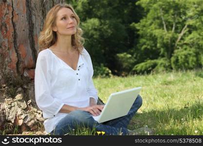 Blond woman sat by tree with laptop deep in thought