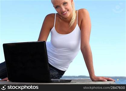 Blond woman sat on jetty with laptop