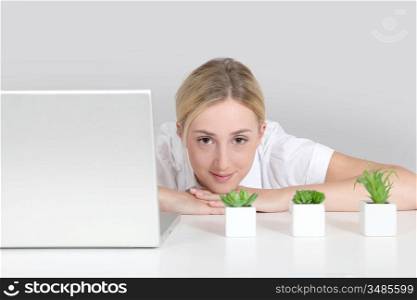 Blond woman sitting by computer and green plants