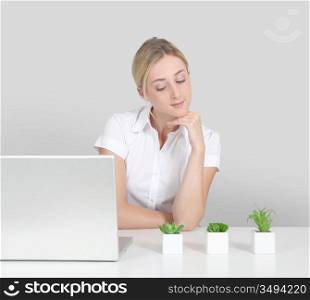 Blond woman sitting by computer and green plants