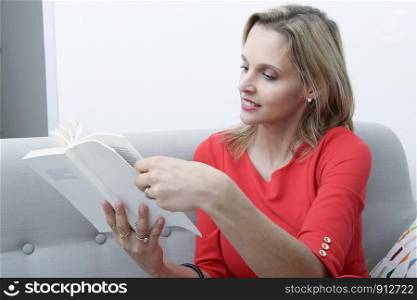 blond woman sitting in the sofa reading a book