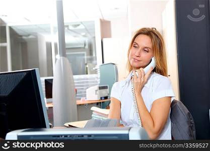Blond woman talking on the phone in front of desk computer