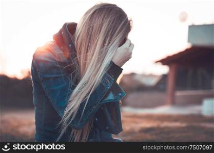 Blond woman wearing jeans jacket standing outdoors in mild sunset light, autumn fashion of youth, urban lifestyle concept