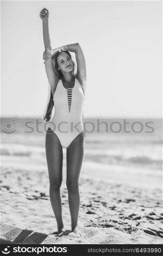 Blond woman with beautiful body in swimswit on a tropical beach. Young blonde woman with beautiful body in white swimsuit on a tropical beach. Caucasian female with straight long hairstyle smiling.