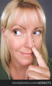 Blond Woman with Finger in Her Nose Against a Grey Background.