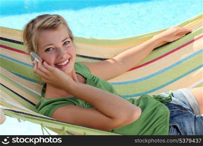 Blond woman with mobile telephone laying in hammock
