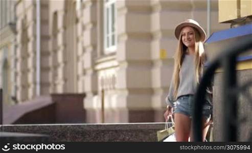 Blond woman with shopping bags walking on the city street and smiling after shopping day
