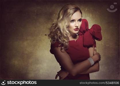 blond young woman in red dress and creative hair style , looking on one side. she has a big bow