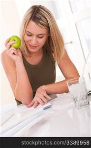 Blond young woman thinking about homework and eating apple