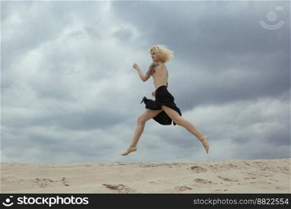 Blonde bare lady running along beach scenic photography. Picture of person with dramatic sky on background. High quality wallpaper. Photo concept for ads, travel blog, magazine, article. Blonde bare lady running along beach scenic photography