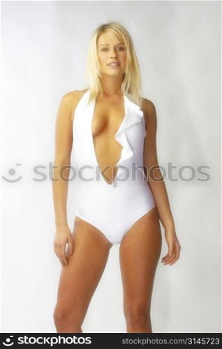 Blonde bombshell wears a white bathing suit in the studio.