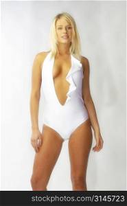 Blonde bombshell wears a white bathing suit in the studio.