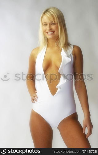 Blonde bombshell wears a white bathing suit in the studio.