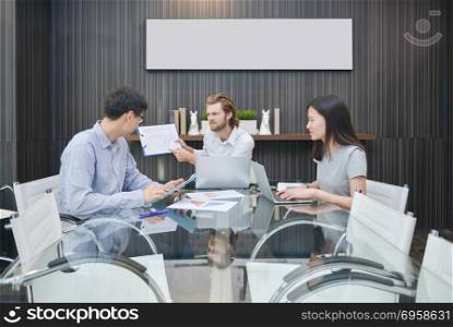 Blonde business man blaming Asian employee in meeting room
