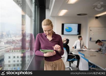Blonde businesswoman in casual clothes working on tablet computer at modern startup business office interior. Young people group on team meeting blured in background