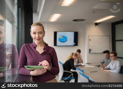 Blonde businesswoman in casual clothes working on tablet computer at modern startup business office interior. Young people group on team meeting blured in background