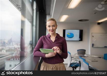Blonde businesswoman in casual clothes working on tablet computer at modern startup business office interior. Young people group on team meeting blured in background