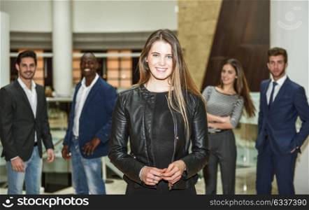 Blonde businesswoman leader looking at camera in office building. Group of multi-ethnic people in the background