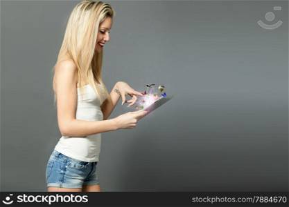 Blonde caucasian woman standing with tablet over grey background