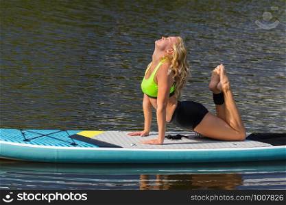 Blonde european woman practices yoga pose on SUP in water
