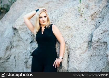 blonde girl in a black trouser suit with blue eyes on the background of a granite quarry from gray rubble