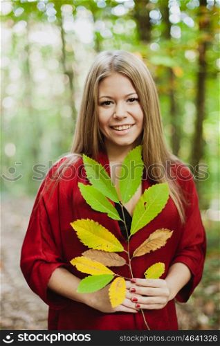 Blonde girl in a misterious forest holding a branch of a tree with autumn colors